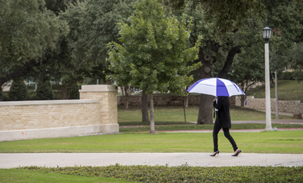 Pedestrian with umbrella walks across campus